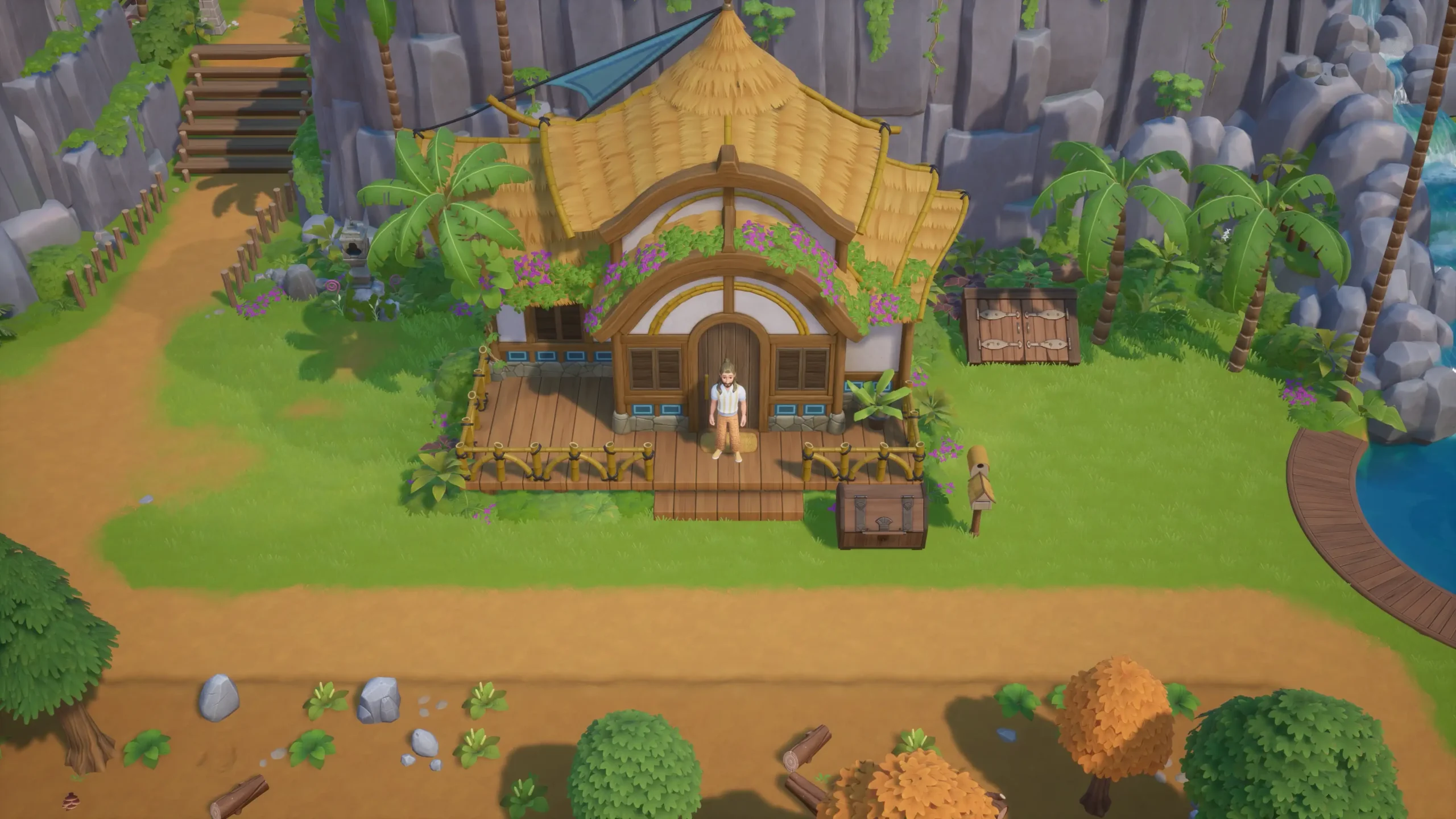 Screenshot from Coral Island showing a character standing on the porch of a thatched-roof house, surrounded by green grass, palm trees, and rocky cliffs on a vibrant island.