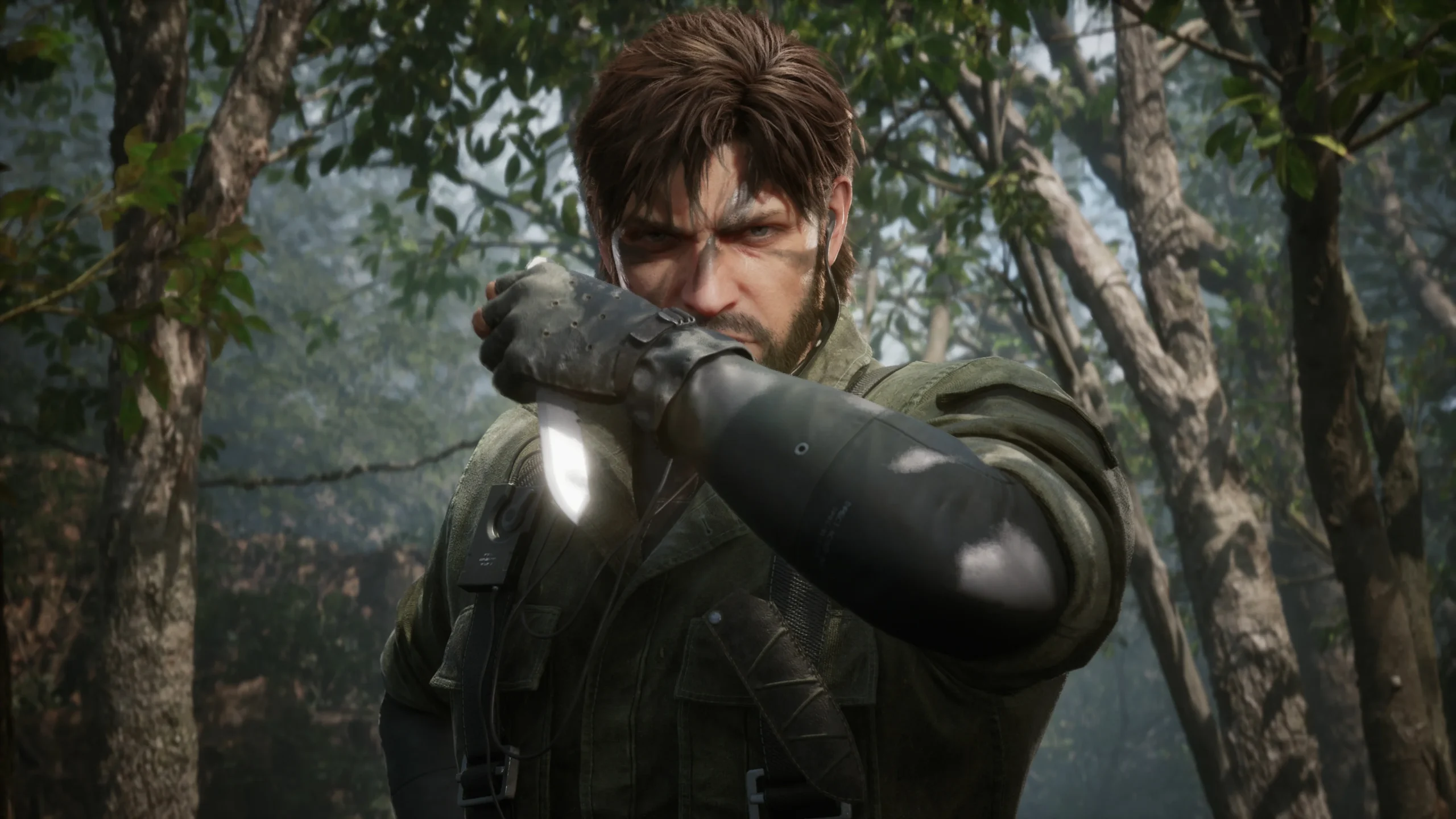 Close-up of Snake from Metal Gear Solid Delta: Snake Eater, in a jungle setting, holding a combat knife across his face. He has a beard and intense eyes.
