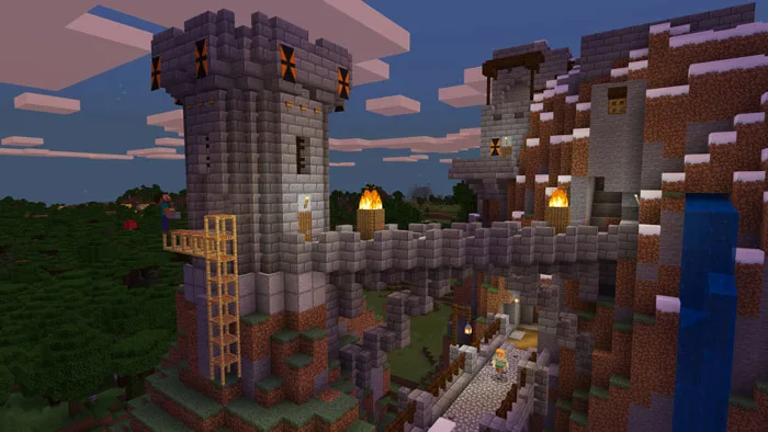 A large, multi-tiered stone castle with torches and wooden scaffolding built into a grassy, snowy mountainside in Minecraft.