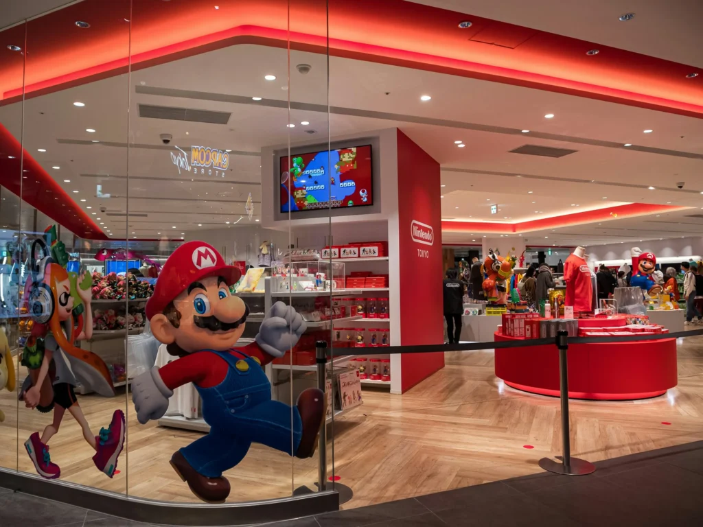 A bright and modern Nintendo store in Tokyo, with a large Mario statue and a Splatoon character cutout in the foreground, visible through a glass exterior.