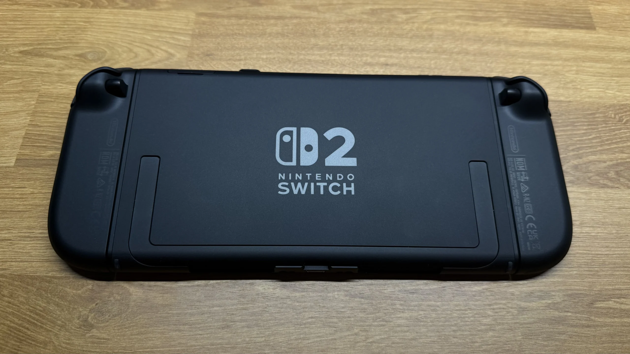 A photo of the back of the Nintendo Switch 2, revealing its matte black finish. The device features a central kickstand area, and the 'Nintendo Switch 2' logo is clearly visible in the center, subtly embossed on the casing. The design suggests a streamlined and possibly more durable build than its predecessor.